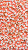 Fresh popcorn scattered on coral pink background, creating dynamic pattern. Fluffy white kernels with golden centers offer contrast for food and entertainment designs.