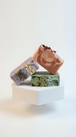 Stack of handmade artisan soap bars with natural ingredients including dried flowers and herbs on clean white background for skincare and wellness.