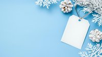 White blank gift tag with pine cones and snowflake decorations on pastel blue background, winter holiday flat lay composition with copy space for text.