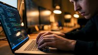Focused programmer coding on laptop in modern office environment with warm ambient lighting during evening work session.