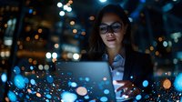 Young Asian businesswoman working on laptop at night in modern office with city lights bokeh background creating professional technology atmosphere.