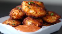 Crispy spiced chicken nuggets with creamy dipping sauce in white ceramic bowl, close-up view showing golden-brown crust and garnished with fresh herbs.