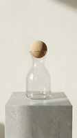 Clear glass bottle with cork sphere stopper on concrete pedestal against neutral background, minimalist home decor and modern interior design styling.