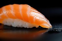 Fresh salmon nigiri sushi piece on dark background with reflection, extreme close up macro shot showing texture of raw fish and rice preparation.