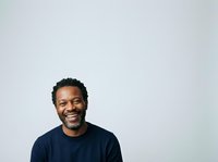 Smiling African American man with dark curly hair wearing navy blue t-shirt against white background. Portrait suitable for corporate, business, lifestyle, and professional website use.