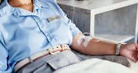 Patient receiving intravenous therapy in hospital bed wearing light blue medical gown with IV drip catheter inserted in arm for medical treatment and care.