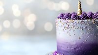 Purple ombre unicorn birthday cake with gold horn, rainbow sprinkles and whipped cream decoration on blurred bokeh background for party celebration.