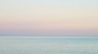 Serene seascape at dawn with soft pastel sky transitioning from pink to blue over calm turquoise waters, ideal for wellness and travel backgrounds.