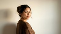 Young Hispanic woman in brown sweater looking over shoulder with warm natural lighting for lifestyle and portrait photography.