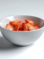 Fresh cooked pink shrimp served in modern white ceramic bowl on light background, close up view of seafood appetizer for restaurant menu and food design.