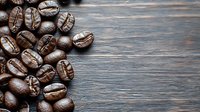 Fresh roasted coffee beans scattered on rustic wooden background with copy space, dark moody lighting creates rich contrast for food photography.