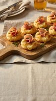 Gourmet puff pastry appetizers topped with prosciutto and herbs on wooden board, elegant party food presentation for catering and entertaining events.