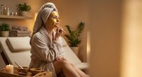 Young woman in bathrobe and towel enjoying spa treatment at home wellness center with golden lighting and relaxing atmosphere for self-care routine.