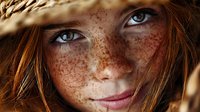 Young redhead woman with freckles and blue eyes wearing straw hat in golden sunlight for natural beauty and summer lifestyle concepts.