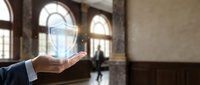 Businessman hand holding glowing lightbulb hologram in modern office lobby representing innovation, creativity and bright ideas for business solutions.