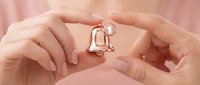 Protective hands forming shelter over small metallic human figure symbolizing care, security, insurance, support and guardianship in soft pink tones.
