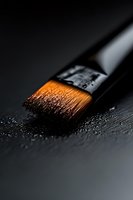 Macro shot of wet paintbrush with orange bristles on dark background, showing fine details and water droplets. Artistic composition highlights craftsmanship and creativity.