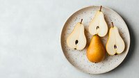 Fresh ripe pears, whole and halved, arranged on speckled ceramic plate against light background. Minimalist food composition with golden fruit.