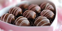 Chocolate truffles with white drizzle arranged in heart shaped box against pink background, selective focus on gourmet confectionery for romantic occasions.