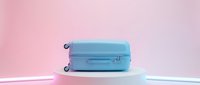Light blue suitcase on a white podium against a soft pink background with neon glow, travel and luggage concept for modern design.