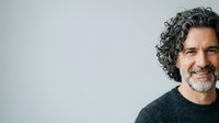 Middle-aged man with curly gray hair and beard, smiling at camera against neutral background. Suitable for business, corporate, lifestyle, and professional website use.
