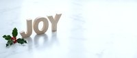 Wooden JOY letters with holly and red berries on white marble surface, festive Christmas holiday decoration with copy space for greeting cards.