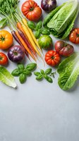 Fresh organic vegetables including heirloom tomatoes, rainbow carrots, romaine lettuce and basil herbs arranged on gray background for healthy cooking.