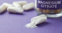 White magnesium citrate capsules spilled on purple surface with supplement bottle label visible for health and wellness concepts.