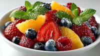 Fresh fruit salad with strawberries, blueberries, raspberries, orange segments and mint leaves in white bowl, colorful healthy dessert.