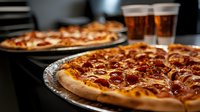 Fresh pepperoni pizza with melted cheese and crispy crust served on aluminum tray alongside cold beer glasses in modern kitchen setting for food delivery.