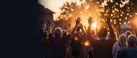 Crowd of people raising hands at outdoor sunset event, golden bokeh lights glowing in background, community celebration or concert atmosphere.