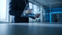 Businessman holding transparent digital tablet displaying financial data analytics and charts in modern office environment for business technology presentations.