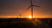 Wind turbines generating renewable energy at sunset with dramatic orange sky and sunburst over rural landscape for sustainable power and environmental concepts.