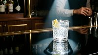 Bartender in white shirt preparing refreshing cocktail with ice and lemon twist on dark bar counter, professional mixology and hospitality service.