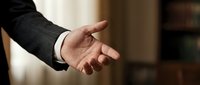Professional businessman extending hand for handshake in formal office setting, representing partnership, agreement, and business cooperation.