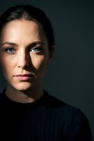 Young Caucasian woman with blue eyes and natural makeup in dark sweater against moody background for professional headshot and portrait photography.