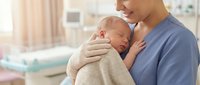 Loving mother gently holding her newborn baby in hospital room, tender bonding moment between parent and infant in medical setting.