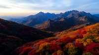 Majestic mountain landscape with vibrant autumn foliage in red and gold colors against dramatic peaks at sunset, creating stunning natural scenery for travel photography.
