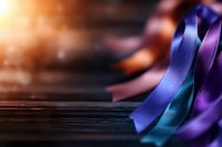 Colorful silk ribbons in blue, purple and turquoise shades lying on dark wooden surface with soft focus and warm light effect, creating elegant composition.