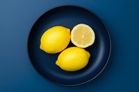 Fresh yellow lemons on a dark navy blue plate, top view flat lay, vibrant color contrast for food and healthy lifestyle concepts.