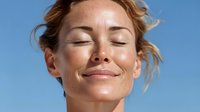 Young woman with freckles enjoying sunshine with eyes closed against clear blue sky, expressing serenity and mindfulness in natural light.