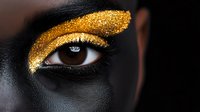 Striking gold glitter eyeshadow makeup on dark skin close up. Dramatic black and gold contrast highlighting creative cosmetic artistry and luxury beauty concept.