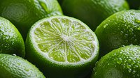 Fresh ripe green limes with water drops, one cut in half showing juicy pulp texture. Macro food photography for healthy eating and cocktail concepts.