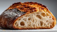 Rustic artisan sourdough bread with golden crust and airy crumb structure, freshly baked and sliced to show texture.