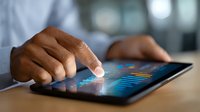 African American businessman analyzing financial data and market trends on digital tablet screen, close up view of hands touching interactive charts.