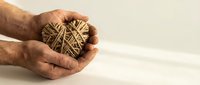 Elderly hands gently holding heart-shaped bundle of natural twine rope on white wooden background. Concept of love, care, crafting and handmade projects.