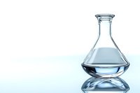 Clear glass laboratory flask containing transparent liquid on reflective surface with soft blue background lighting creates scientific atmosphere.