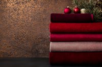 Stack of soft folded towels in red and pink tones with Christmas ornaments and pine branches on rustic background.