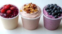 Creamy yogurt parfaits topped with fresh raspberries, crunchy granola, and blueberries in white cups. Healthy breakfast or dessert options with smooth texture and vibrant colors.