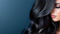 Young woman with luxurious dark wavy hair and professional makeup against blue background, showcasing healthy shiny hairstyle and beauty treatment results.